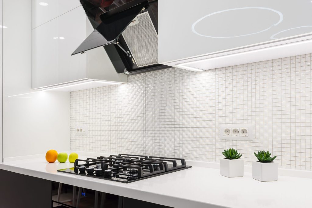 A white kitchen with a mosaic splashback, angled hood and gas cooktop.