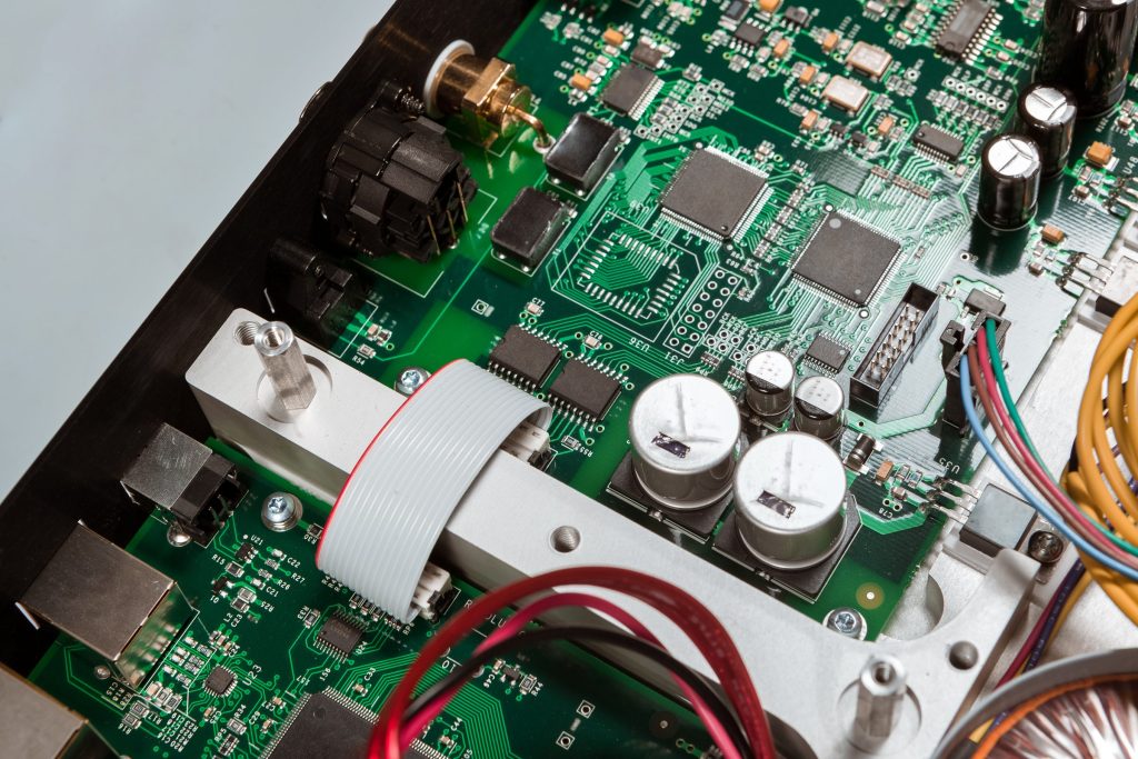 A green control board at an angle, ribbon cable across it, electrolytic capacitors and two square controllers.