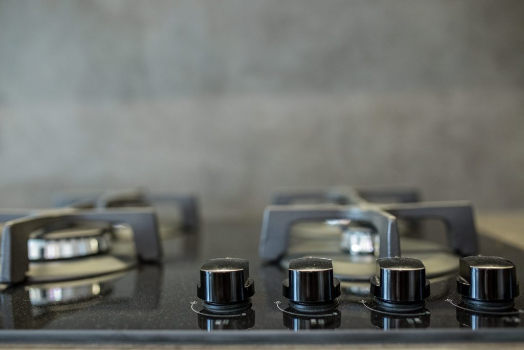 Four control knobs along the front edge of a dark gas hob, cast grates behind them out of focus.
