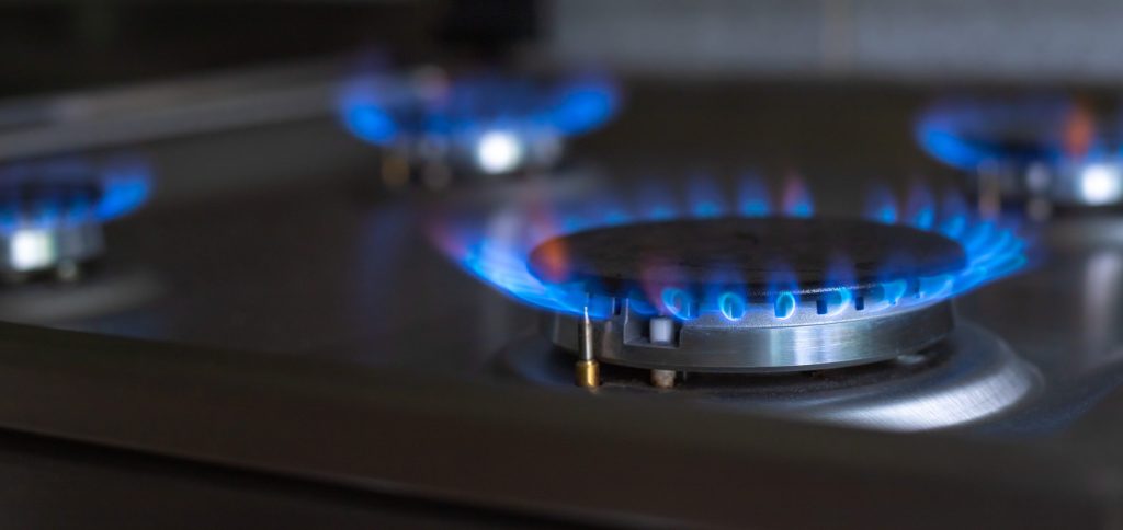 Three gas burners alight on a dark cooktop, the igniter electrode visible at the ring