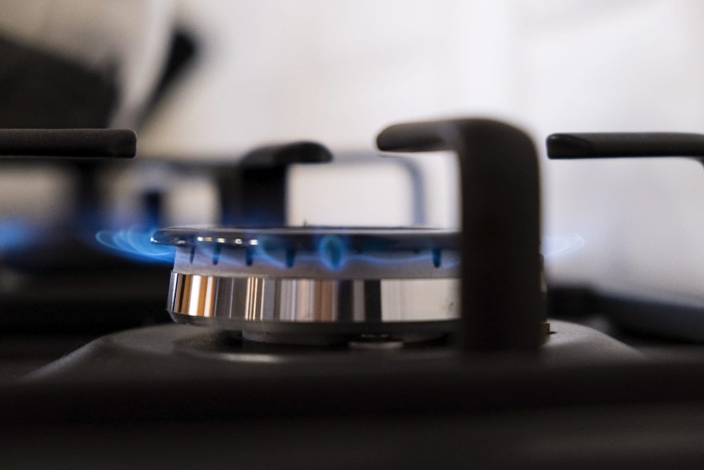 A gas burner alight beneath a heavy cast iron grate on a range