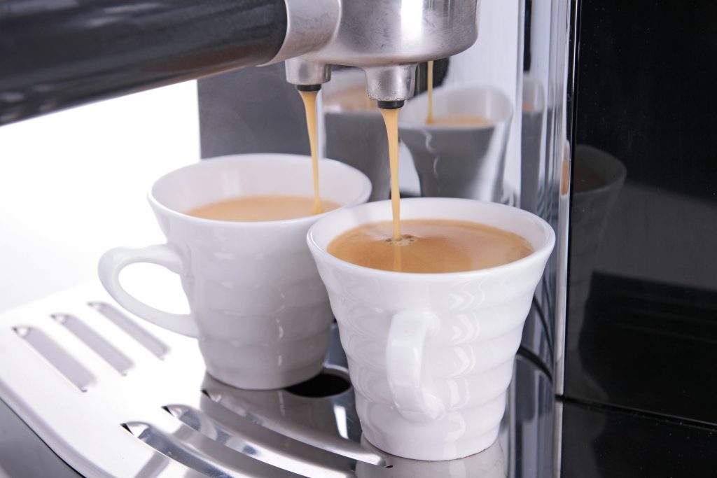 Espresso running from the twin spout of an automatic coffee machine into two white cups