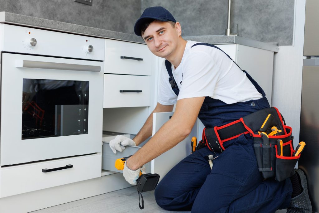 A fitter with a cordless driver working at a drawer beside a built-in oven column