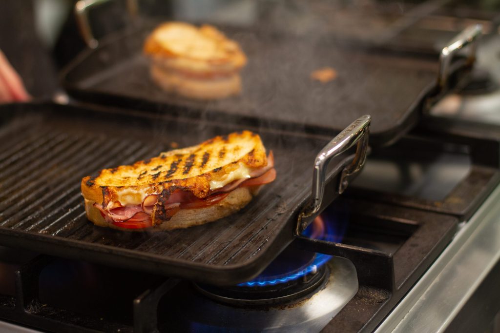 A cast griddle plate over a lit gas burner with a sandwich toasting on it