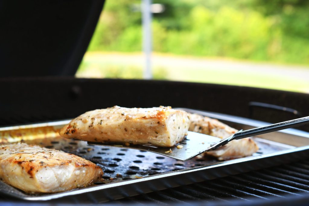 Fish cooking on a perforated tray over the grate of an outdoor gas grill