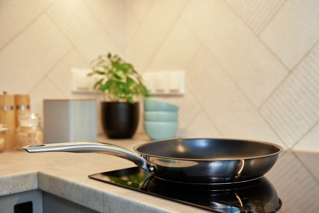 A frying pan resting on the black glass surface of a cooktop.