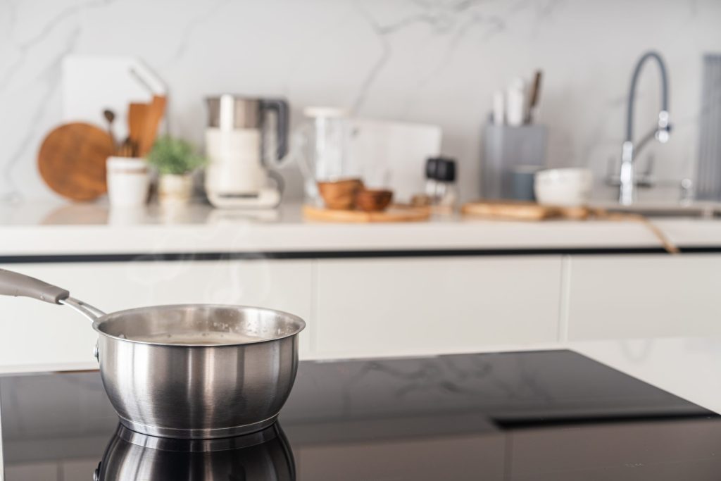 A steel saucepan steaming on a black induction cooktop.