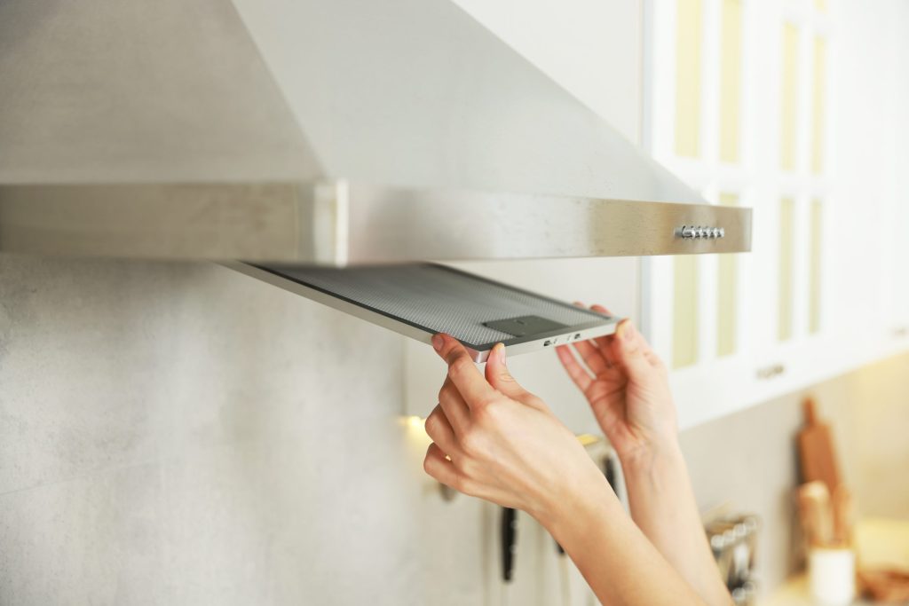 Two hands lifting the metal grease filter out of a range hood.