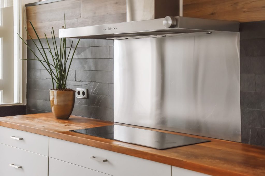 A stainless range hood above an induction hob set into a wooden worktop