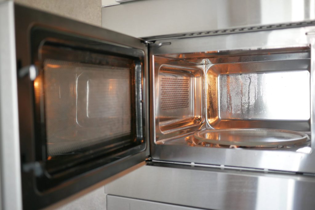 A microwave standing open, its stainless cavity and turntable clean and empty
