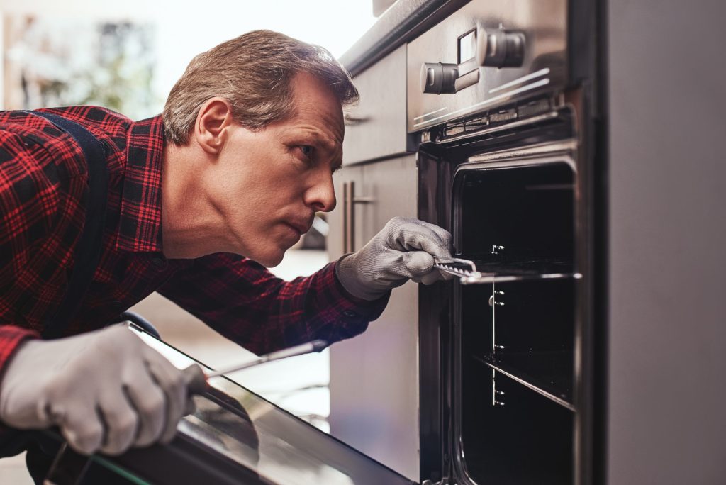 A technician holding the oven door glass in one hand and working at the open door with the other