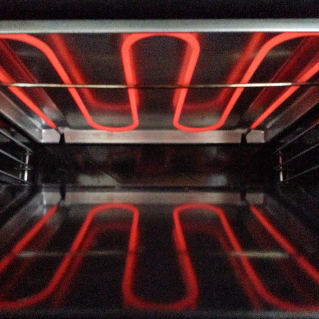 The inside of an oven with the top and bottom elements at red heat, racks between them.