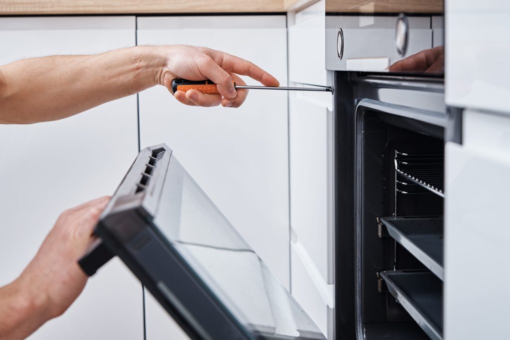 Hands easing the control fascia away from a built-in oven with a screwdriver