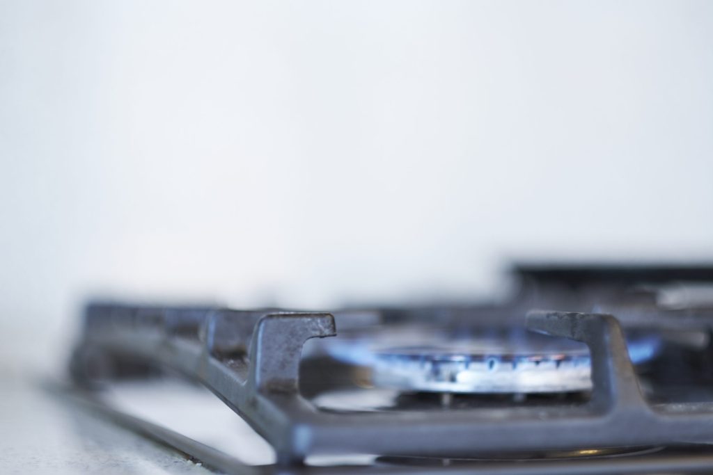 A burner simmering low under the steel grate of a sealed burner rangetop