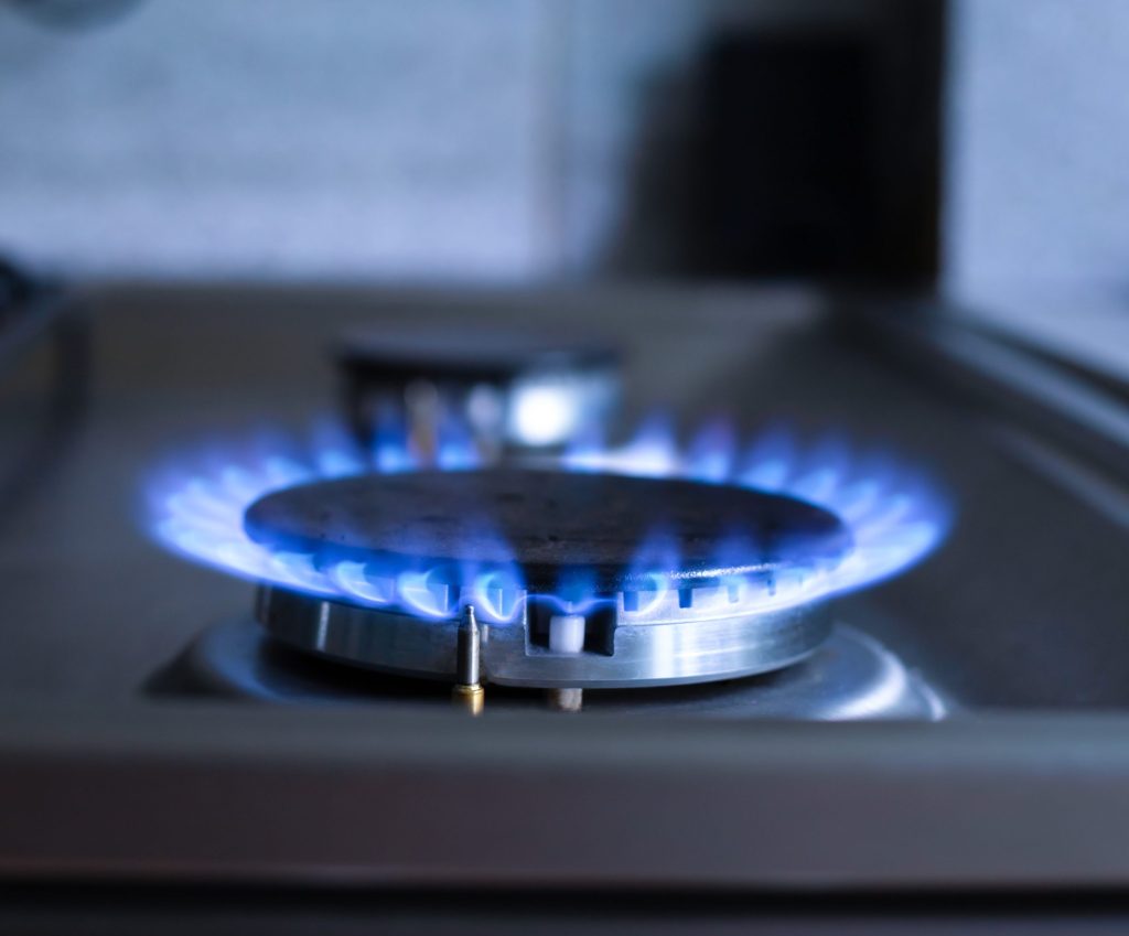 A single gas burner alight with a low even blue flame, close up in a dark kitchen