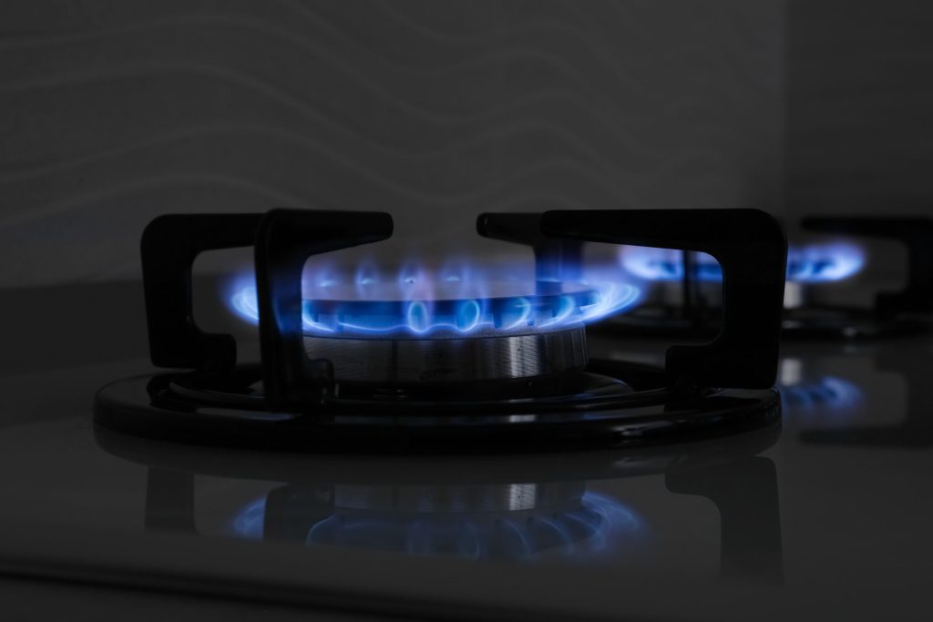 Two burners alight at a low setting on a dark gas hob, blue flames reflected in the surface