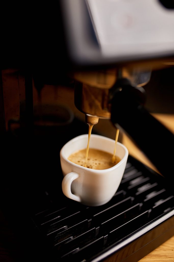 Espresso pouring from a machine spout into a white cup on a dark drip tray