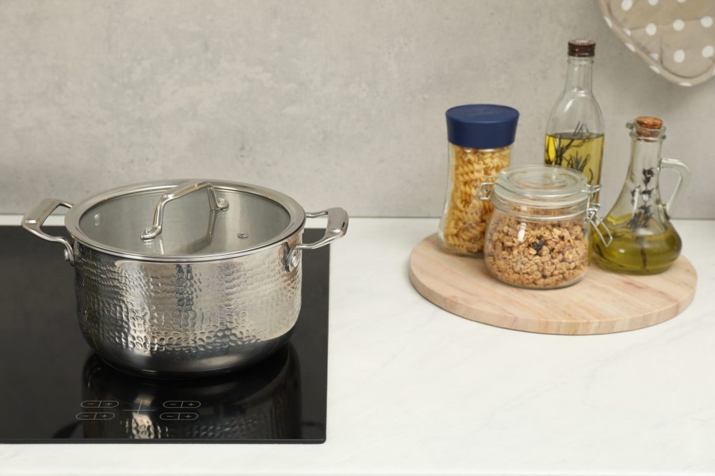 A lidded steel pot standing on a black induction cooktop beside the worktop