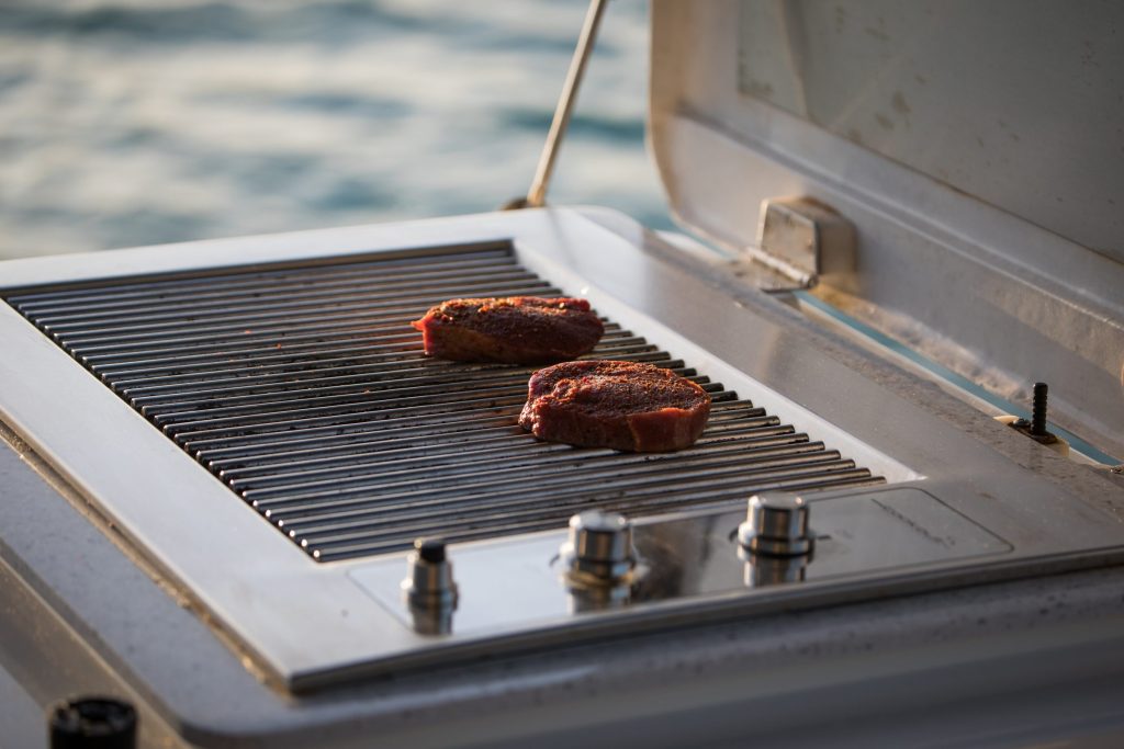 Two steaks on one half of a gas grill grate, the rest of the grate empty, water behind