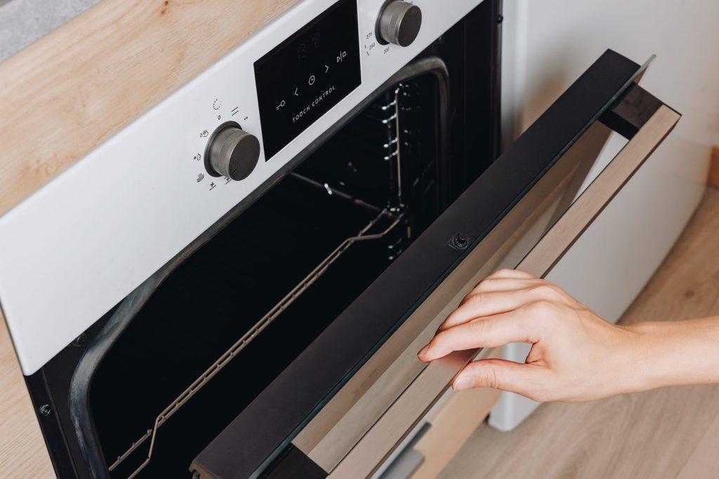 A hand on the handle of a white built-in oven, drawing the door open
