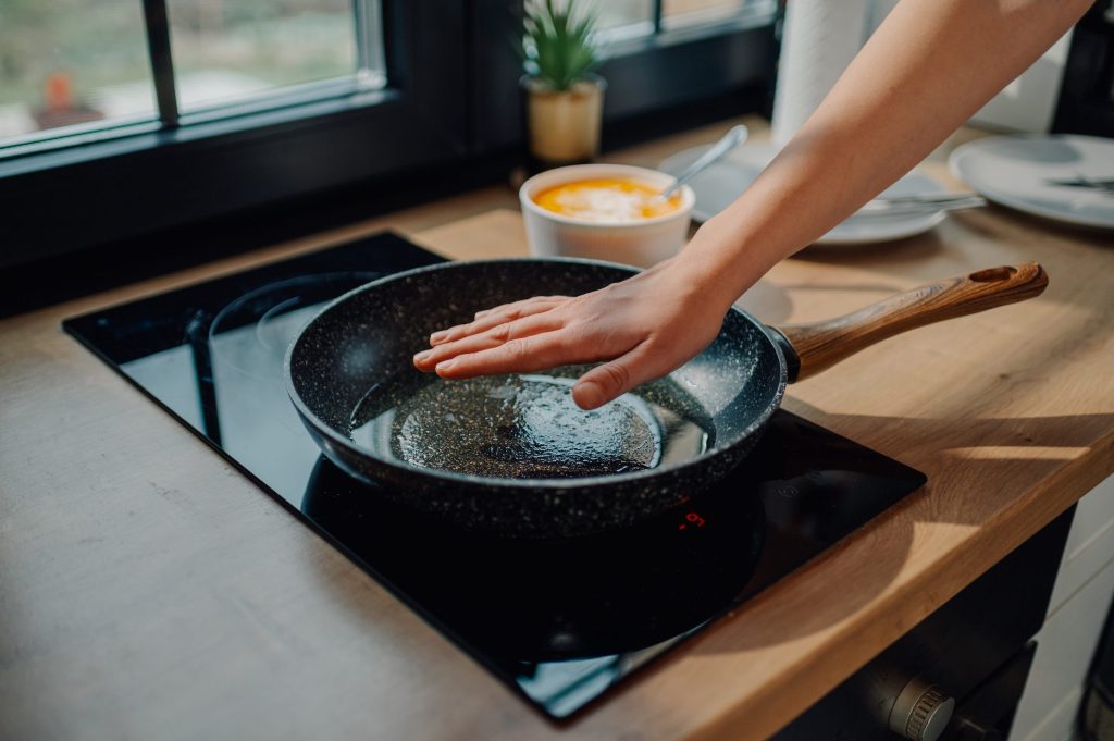 A hand held over a frying pan on a black induction cooktop.