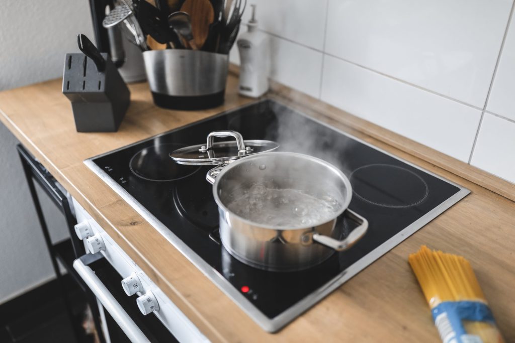 A steel pot boiling on a black cooktop set into a wooden worktop.