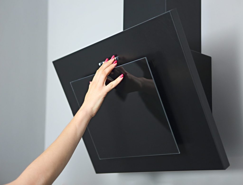 A hand reaching to the glass panel of an angled black range hood.