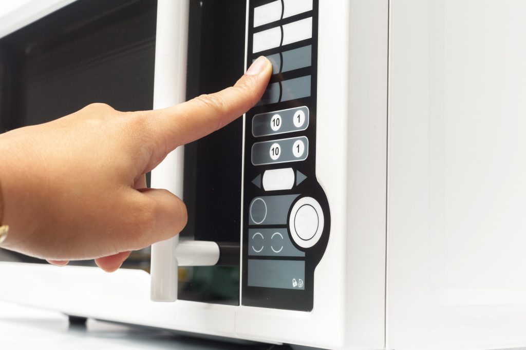 A finger pressing one of the membrane keys on a white microwave keypad
