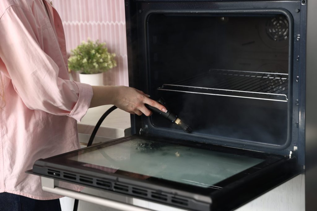 Someone cleaning the inside of an oven with a steam lance, the door lowered