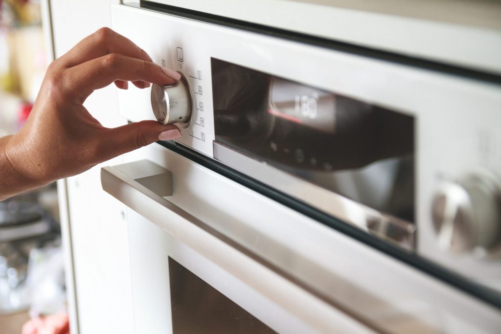 A hand on the control dial of a wall oven whose display reads 180.