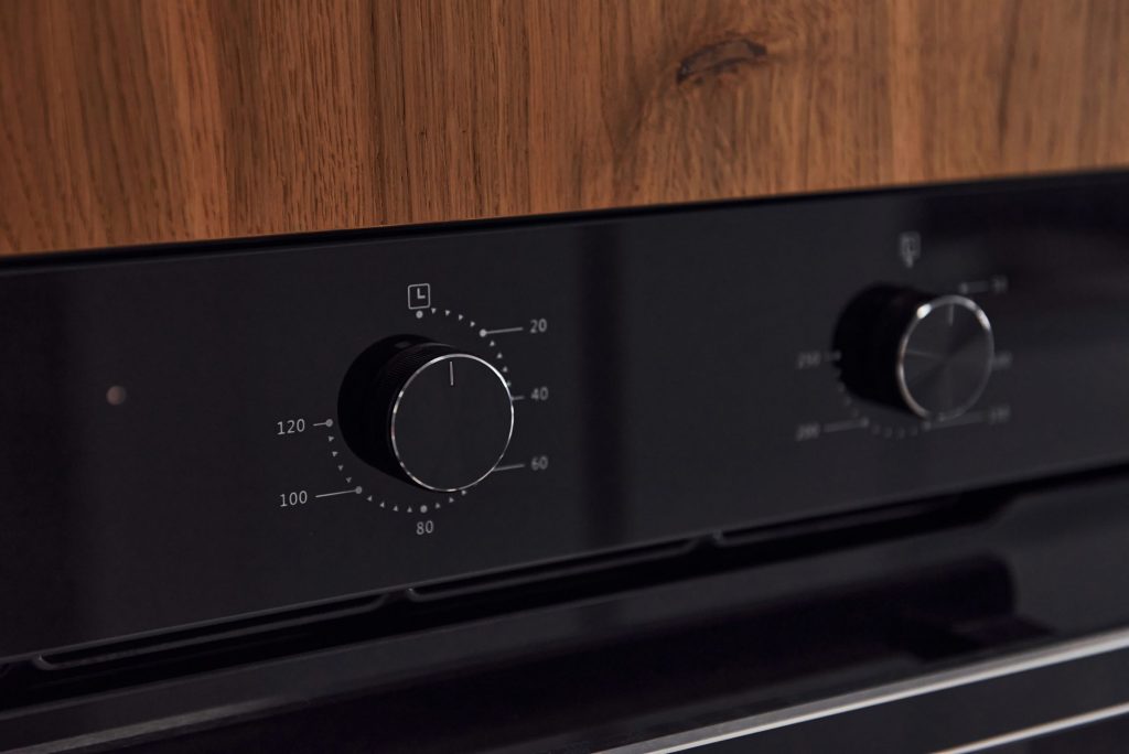 The black control panel of a built-in oven in walnut cabinetry, two dials marked with a temperature scale