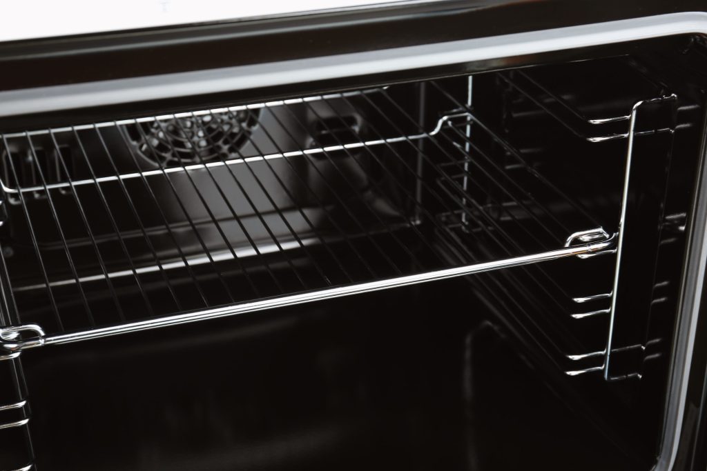 The back wall of a black oven cavity, the round convection fan cover behind the rack