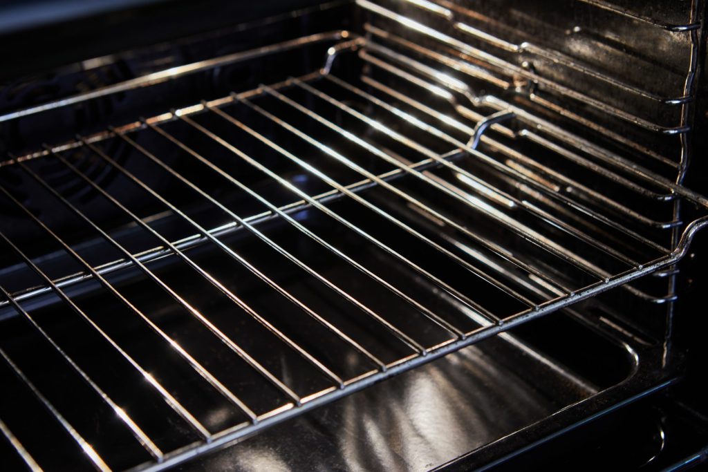 A clean chrome rack in a dark enamel oven, side rails lit from the door.