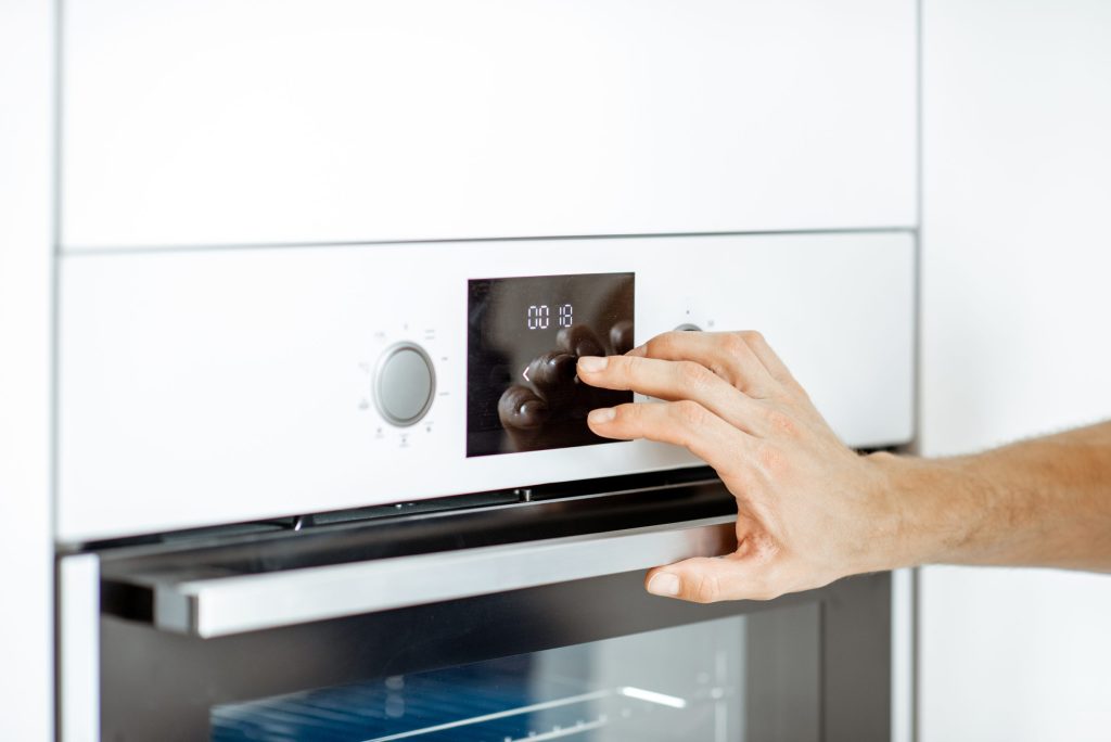 A hand at the small display of a white built-in oven, setting it from the panel