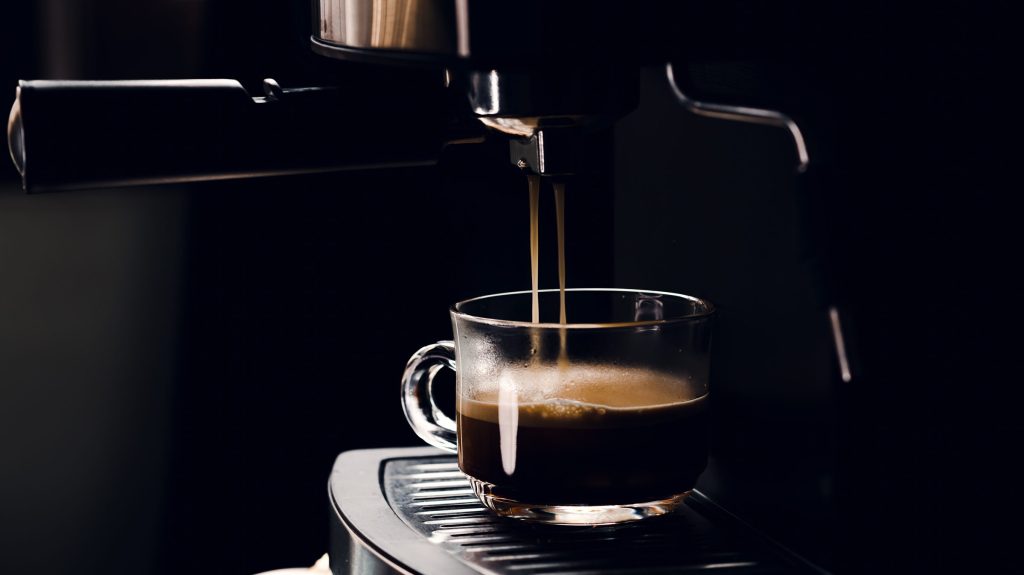 Espresso running from a coffee machine into a glass cup, dark surround