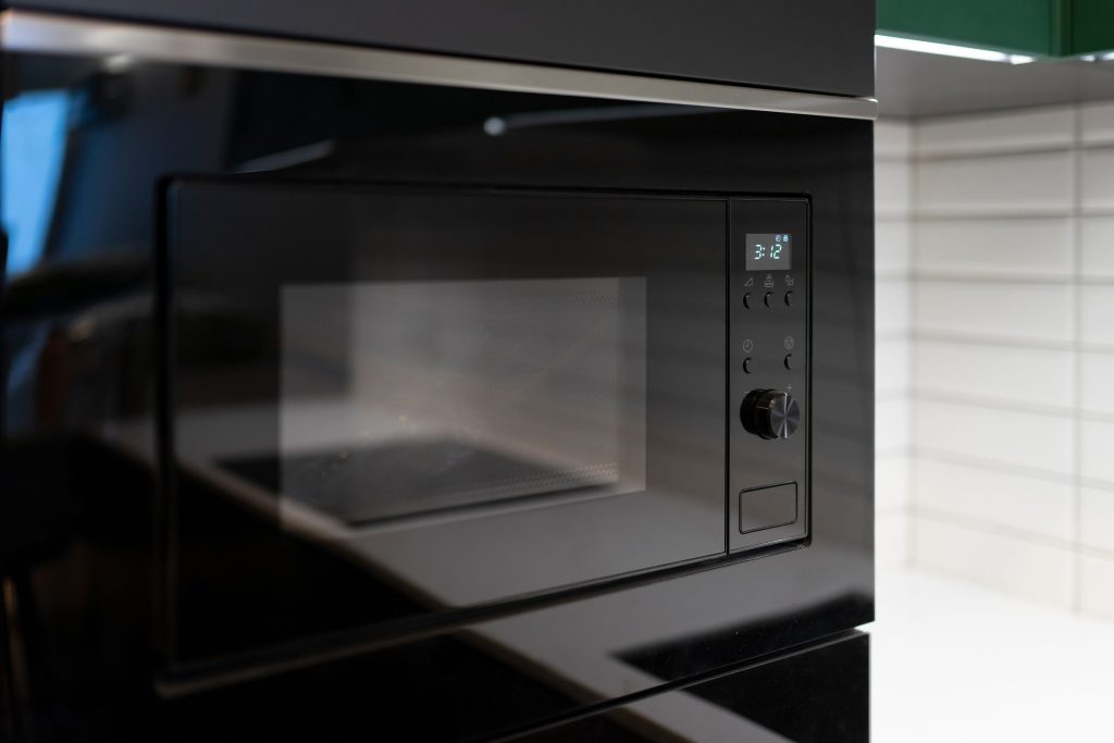A black built-in microwave set into a cabinet, its display lit and counting down