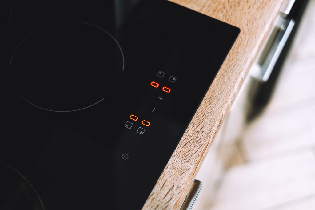 A black induction cooktop set into a wooden worktop, zone indicators lit red beside the touch controls