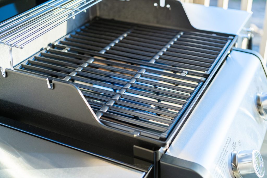 The grates and burner deck of a stainless gas grill, lid raised, seen close